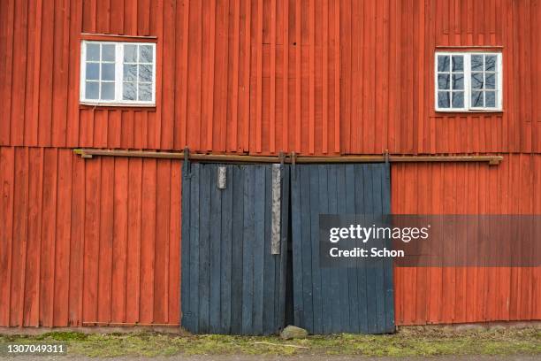 a red wooden facade of a barn with two windows and a black gate - röd lada bildbanksfoton och bilder