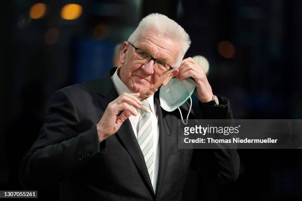 Winfried Kretschmann, premier of Baden-Wuerttemberg and member of the German Greens Party, takes off his face mask before speaking to the media...