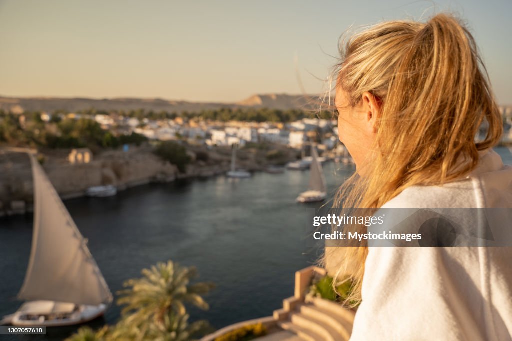 Woman contemplates the Nile river from a balcony, felucca boat