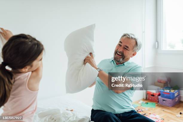 senior man and his granddaughter playing a pillow fight at home - pillow fight stock pictures, royalty-free photos & images