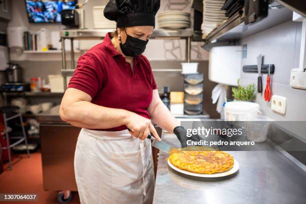cook cutting a potato omelette inside the restaurant kitchen - tortilla de patata fotografías e imágenes de stock