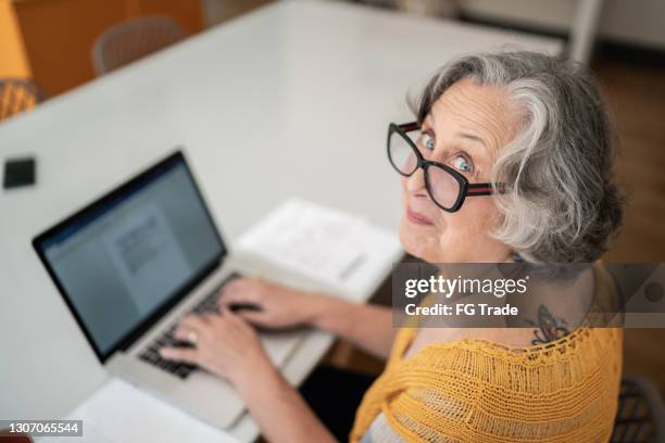 portrait of a senior woman typing on laptop at home - old woman tattoos stock pictures, royalty-free photos & images