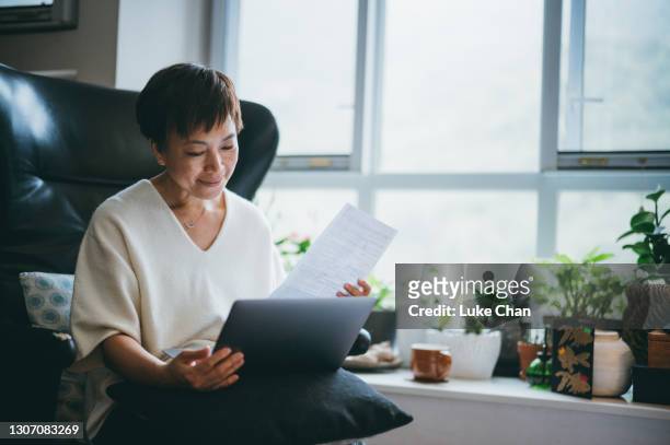 femme asiatique aînée sérieuse en vérifiant des factures, calculant des dépenses devant l’ordinateur à la maison - pension de retraite photos et images de collection