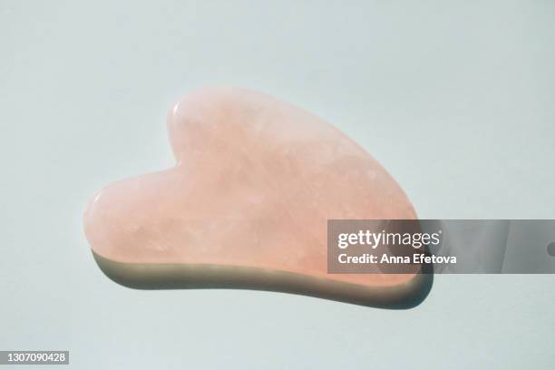 rose quartz guasha for facial massage on light blue teal background with shadow. massagers are typically used for anti aging procedures with an oil or moisturizer. concept of health spa and wellbeing. flat lay style with copy space. cosmetic banner - spooning stock pictures, royalty-free photos & images