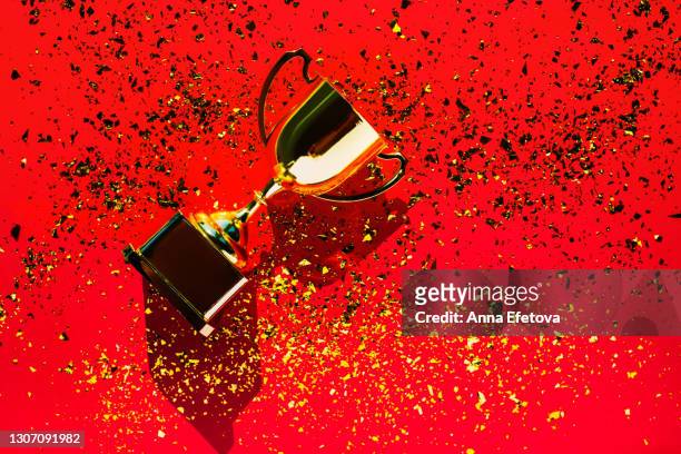 top view of metallic golden winner's cup or goblet on bright red background with sequin. goal achievement concept. trendy colors of the year - gold trophy stock pictures, royalty-free photos & images