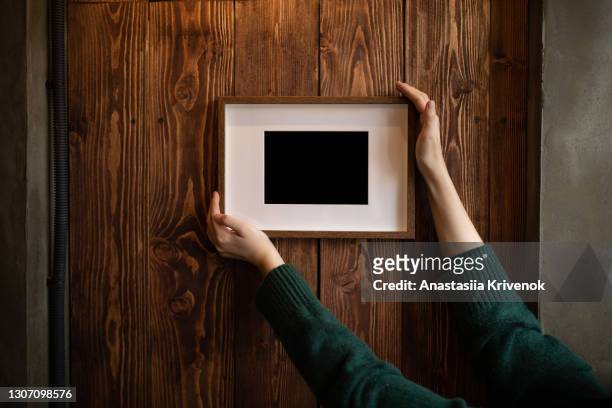 woman's hands holding and supporting picture frame on the wall. - manos pintadas fotografías e imágenes de stock