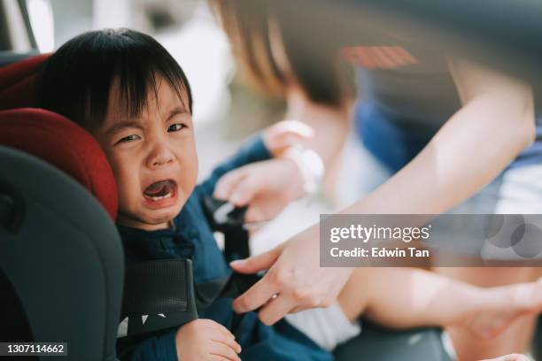 asian chinese mother fastening  buckle up for her baby boy in the car seat - angry babies stock pictures, royalty-free photos & images