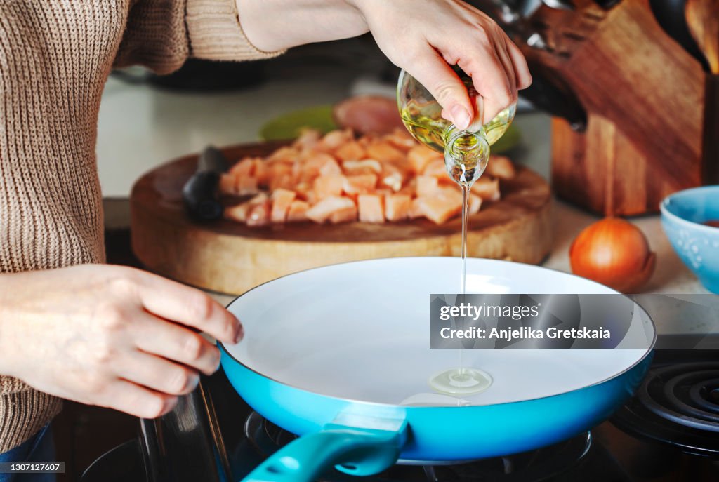 Woman pouring olive oil into the skillet.
