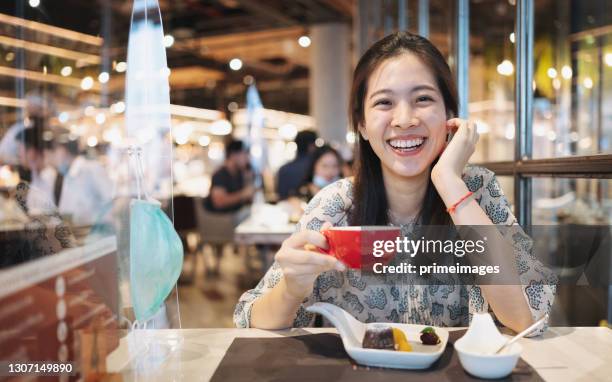 asian woman sitting separated in restaurant eating food .keep social distance for protect infection with hanging ppe protect other from coronavirus covid-19, restaurant and social distancing concept. - food court stock pictures, royalty-free photos & images