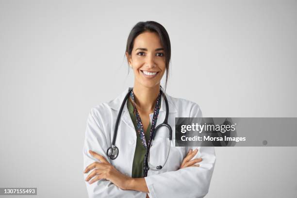 confident mixed race doctor with arms crossed against white background - doctor standing foto e immagini stock