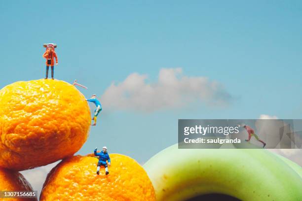 human figurines climbing tangerines and bananas against sky with clouds - menschliche darstellung stock-fotos und bilder