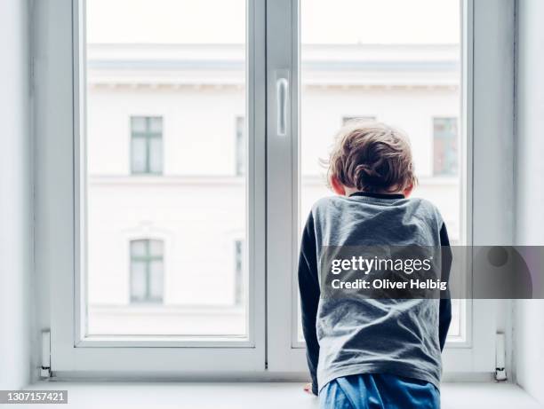 sad little boy looks out the window. he is not allowed to meet or visit friends during lockdown or quarantine - solo bambini maschi foto e immagini stock