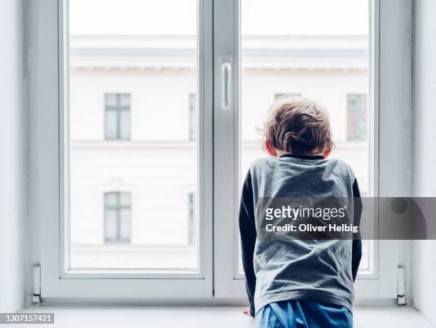 sad little boy looks out the window. he is not allowed to meet or visit friends during lockdown or quarantine - losing virginity - fotografias e filmes do acervo