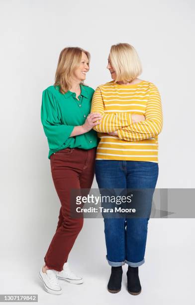 two mature female friends standing together - two people plain background stock pictures, royalty-free photos & images