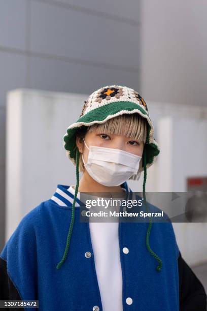Guest is seen on the street wearing colorful design knit bucket hat and pants, neon green Mikio Sakabe sneakers, military graphic blue tote bag, blue...