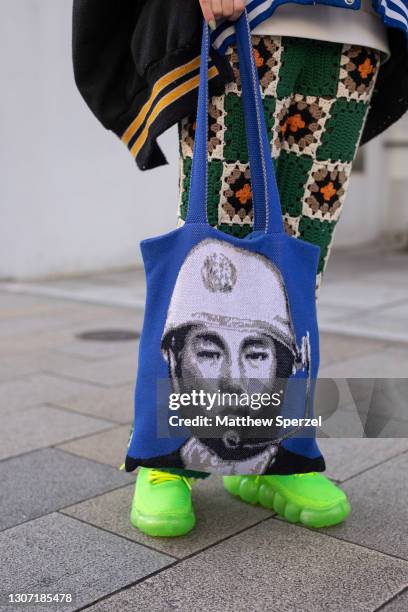 Guest is seen on the street wearing colorful design knit bucket hat and pants, neon green Mikio Sakabe sneakers, military graphic blue tote bag, blue...