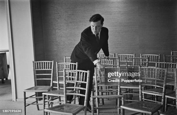 English fashion designer Norman Hartnell arranges chairs for guests invited to view a showing of his Utility clothing fashion range at his salon in...