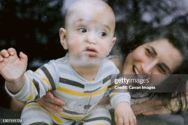 funny baby and mommy at rainy window during quarantine - month stock pictures, royalty-free photos & images