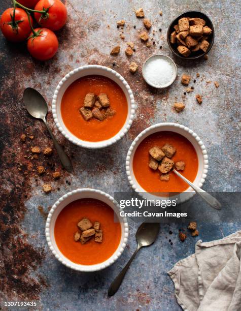 overhead flat lay of bowls of tomato soup on gray stone background. - crouton stockfoto's en -beelden