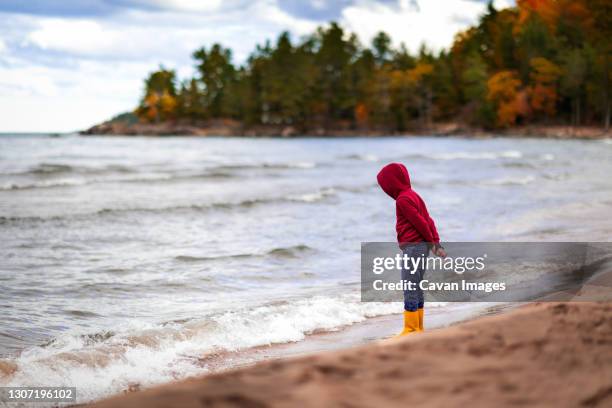 boy standing on shore line of lake superior looking down at water - michigan meer stockfoto's en -beelden