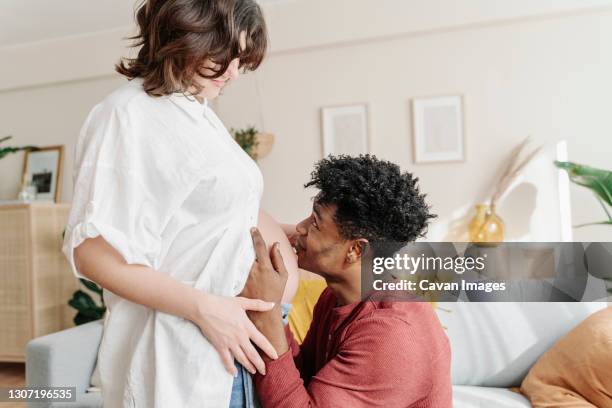 tender black man kissing tummy of pregnant woman - belly kissing stockfoto's en -beelden