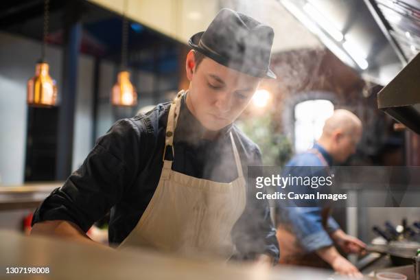 young man cooking in restaurant kitchen - chef smelling food stockfoto's en -beelden