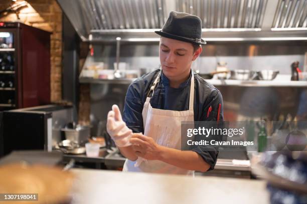 male cook putting on gloves in kitchen - chefs hat ストックフォトと画像