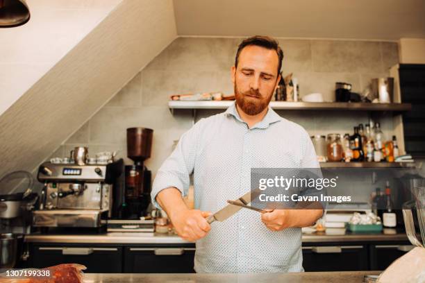 man with beard and moustache sharpening knife, working in restaurant - kitchen knife stockfoto's en -beelden