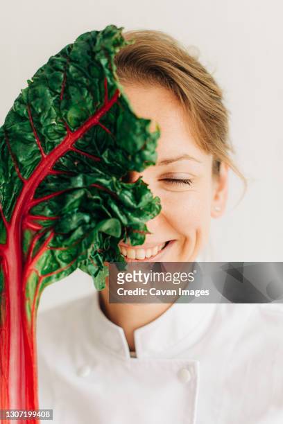 female chef covering face with swiss chard leaf while laughing - woman laugh cook stock pictures, royalty-free photos & images