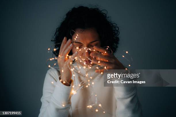 woman with curly hair holding string lights on dark background - tangled christmas lights stock-fotos und bilder