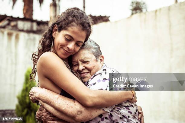 mexican women smile in loving hug embrace on summer street mecxico - hispanic grandmother stock pictures, royalty-free photos & images