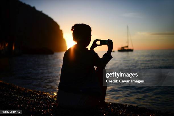 silhouette of a young woman using a smartphone to capture sunset - zuid europa stockfoto's en -beelden