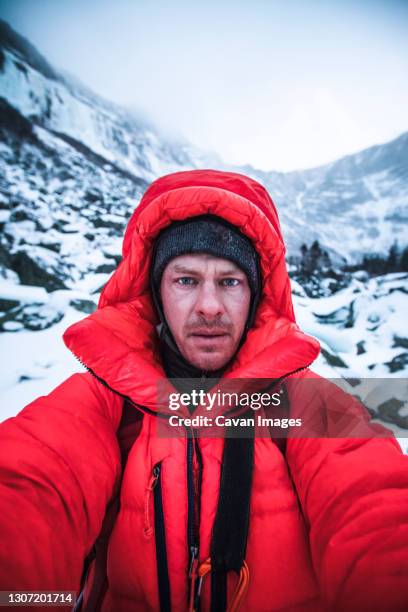 man wearing red puffy jacket takes selfie in very cold conditions. - red coat stock-fotos und bilder