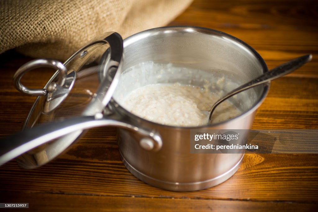 Sweet boiled oatmeal in a saucepan with a spoon