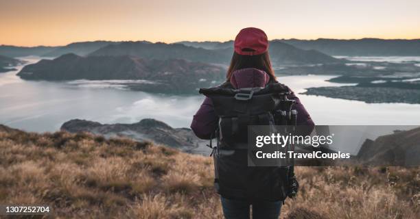 woman hiker on a top of a mountain. fit young woman hiking in the mountains standing on a rocky summit ridge with backpack and pole looking out over an alpine landscape - wanaka stock-fotos und bilder