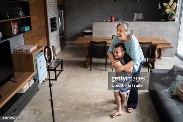 young man with dwarfism and his mother embracing while vlogging at home - mother media call stock pictures, royalty-free photos & images