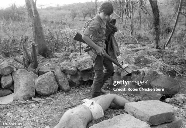 Member of the leftist guerrilla group Fuerzas Populares de Liberacion, FPL, walks past a dead Salvadoran army soldier following an overnight ambush...