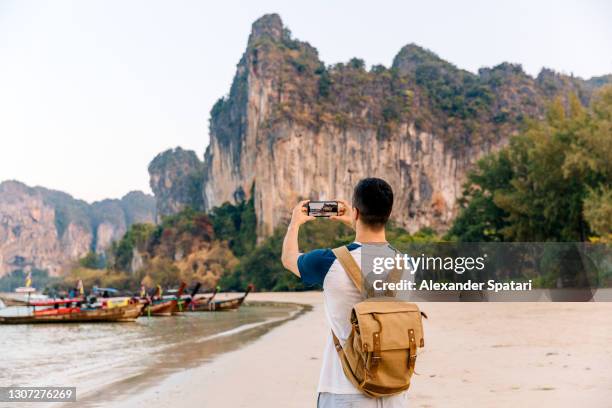 traveller with backpack photographing mountains at the beach using smartphone, krabi, thailand - asian photographer stock pictures, royalty-free photos & images