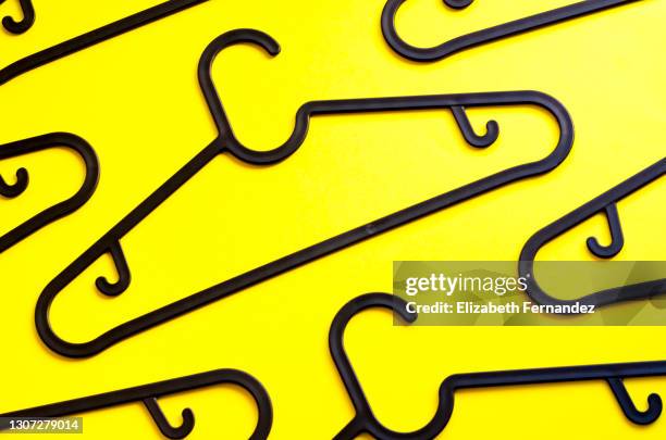 pattern of black plastic hangers on a yellow background. the concept of selling goods, shopping and retail. - coat hanger stock pictures, royalty-free photos & images