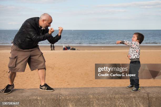 a father plays boxing with his child near the beach in portobello promenade, edinburgh, scotland, uk - funny boxing bildbanksfoton och bilder