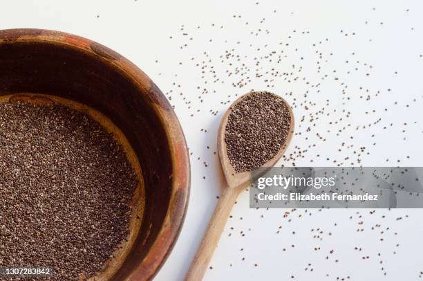 clay vessel and wooden spoon with chia seeds on white background, seeds scattered on the table - chiasamen stock-fotos und bilder