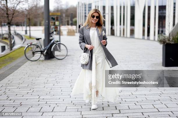 Influencer Gitta Banko wearing a grey blazer with a white lace flower pocket square by Brunello Cucinelli, a long white dress with lace details by...