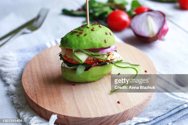 healthy vegan meal: avocado burger with cucumber, tomato, onion, greens and seeds on wooden plate. concept of veganism. - veganisme stock pictures, royalty-free photos & images