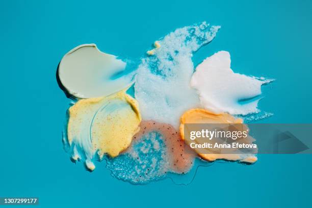 set of textured smears of cosmetic products. herbal green cream, yellow scrub with exfoliating particles, white scrub with coconut oil and sugar, red fruit scrub and orange shower gel on bright blue background. concept of trendy body care procedures of th - clear skin red background stock pictures, royalty-free photos & images