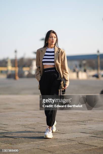 Model wears a beige oversize blazer jacket from Cos, a black and white stripe crop top from Zara, a Dior bag with printed monograms, black sportswear...