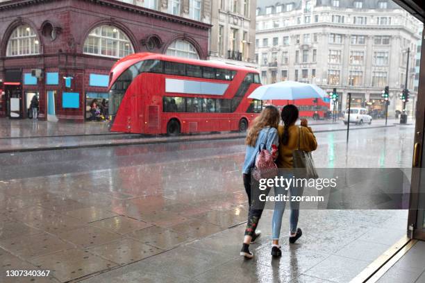 rear view of two women under one umbrella walking the sidewalk in london downtown - shower stock pictures, royalty-free photos & images