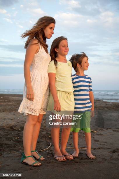 three siblings standing on the beach in descending order, windy day - 13 year old girls in shorts stock pictures, royalty-free photos & images