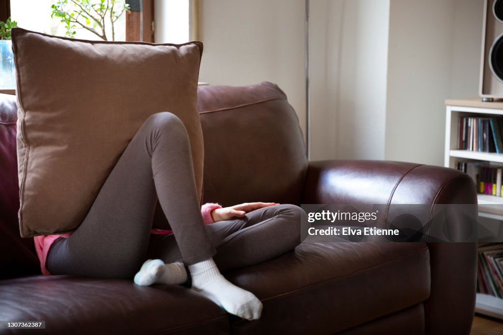 Teenager hiding face behind a large cushion on a sofa