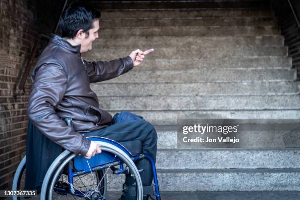 angry handicapped man with one finger up sitting in his wheelchair in front of stairs he can't climb. - at & t center stock-fotos und bilder