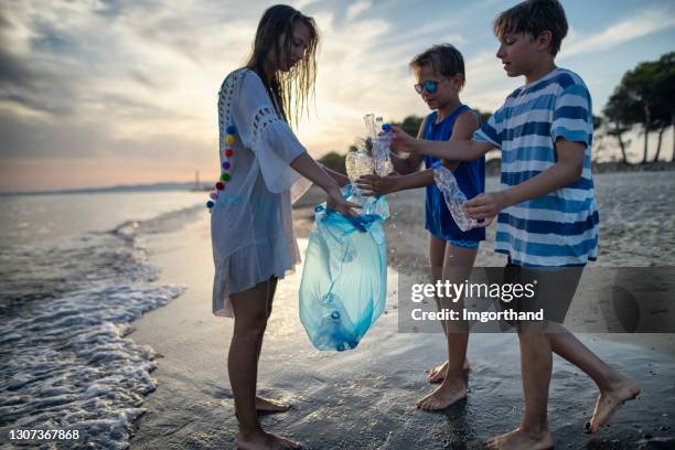 three kids cleaning up the beach - picking up garbage stock pictures, royalty-free photos & images
